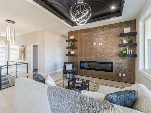 living room featuring an inviting chandelier, a tray ceiling, a tile fireplace, and light hardwood / wood-style flooring