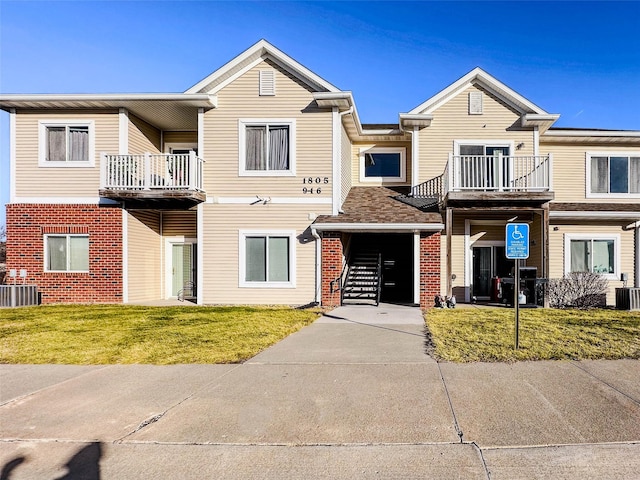 multi unit property featuring a garage, a balcony, a front yard, and central AC unit