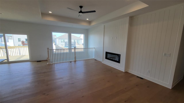 unfurnished living room featuring a tray ceiling, a healthy amount of sunlight, wood finished floors, and visible vents