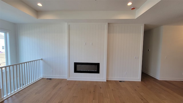 unfurnished living room featuring a tray ceiling, baseboards, light wood finished floors, and a large fireplace