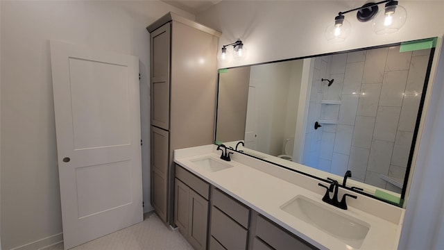 bathroom featuring double vanity, toilet, a tile shower, and a sink