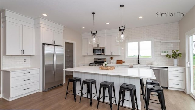 kitchen with sink, hanging light fixtures, a kitchen island, stainless steel appliances, and white cabinets