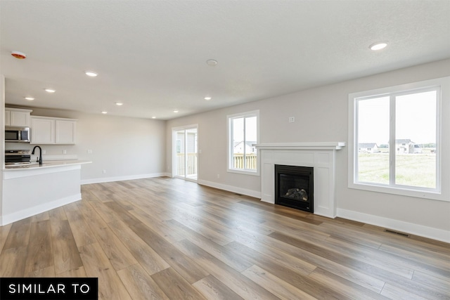 unfurnished living room featuring sink, a wealth of natural light, and light hardwood / wood-style flooring