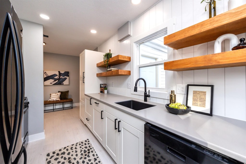 kitchen featuring sink, black appliances, light hardwood / wood-style floors, and white cabinets