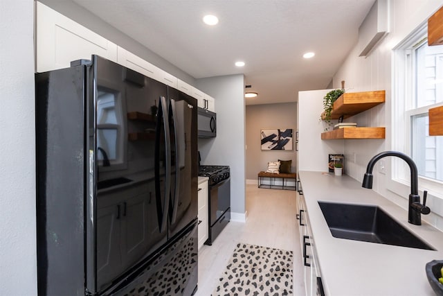 kitchen featuring white cabinetry, sink, light wood-type flooring, and black appliances