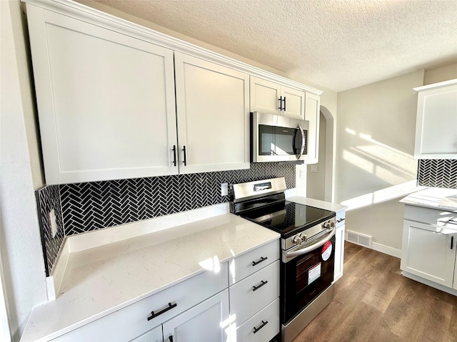 kitchen with white cabinetry, appliances with stainless steel finishes, light stone countertops, light hardwood / wood-style floors, and backsplash