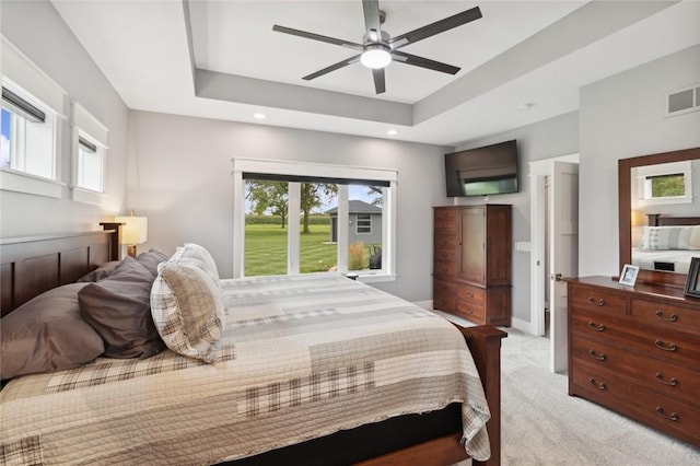 bedroom with ceiling fan, light colored carpet, and a raised ceiling