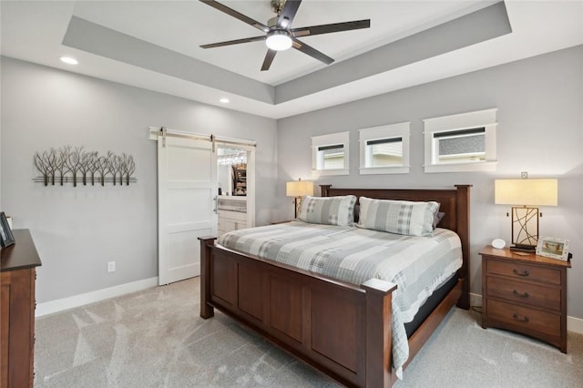 carpeted bedroom featuring connected bathroom, a tray ceiling, a barn door, and ceiling fan