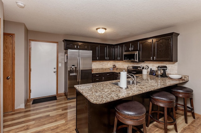 kitchen with dark brown cabinetry, sink, stainless steel appliances, and light wood-type flooring