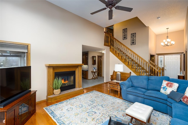 living room with ceiling fan with notable chandelier, a glass covered fireplace, stairway, a high ceiling, and light wood finished floors