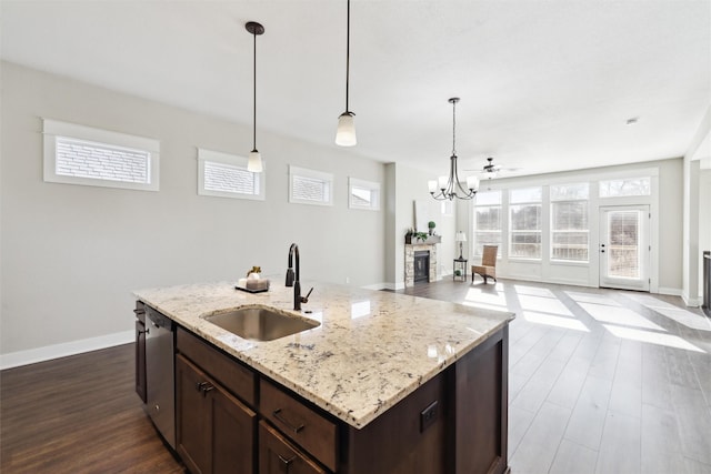 kitchen with stainless steel dishwasher, light stone countertops, sink, and a center island with sink