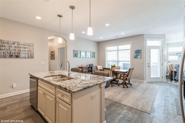 kitchen featuring pendant lighting, sink, dishwasher, light stone countertops, and an island with sink