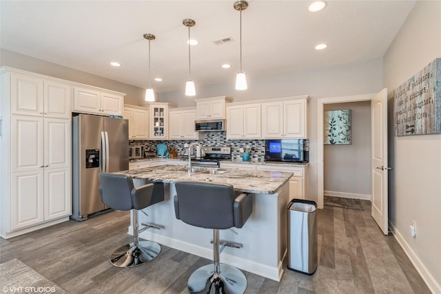 kitchen featuring pendant lighting, an island with sink, white cabinetry, light stone counters, and stainless steel appliances