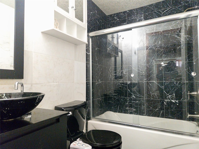 full bathroom with tile walls, enclosed tub / shower combo, vanity, toilet, and a textured ceiling