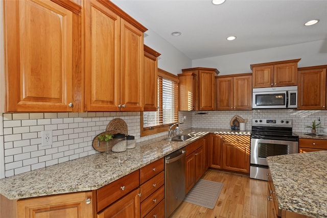 kitchen with appliances with stainless steel finishes, tasteful backsplash, sink, light hardwood / wood-style floors, and light stone countertops