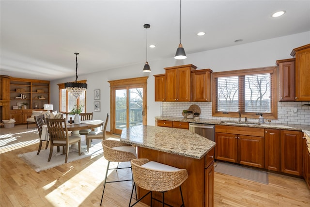 kitchen featuring sink, decorative light fixtures, a center island, dishwasher, and light stone countertops