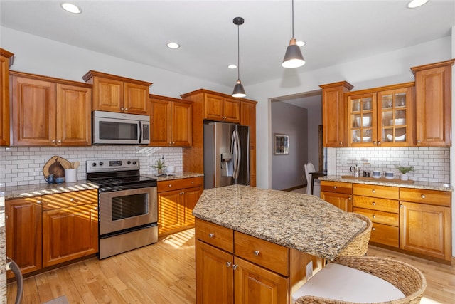 kitchen with appliances with stainless steel finishes, a center island, light stone countertops, decorative light fixtures, and light wood-type flooring