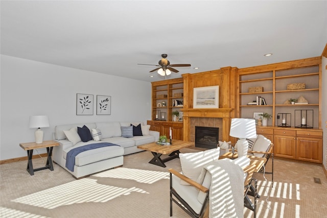 living room featuring light carpet, built in shelves, a fireplace, and ceiling fan