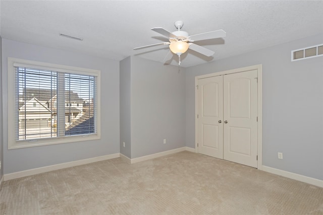 unfurnished bedroom featuring ceiling fan, a closet, light carpet, and a textured ceiling