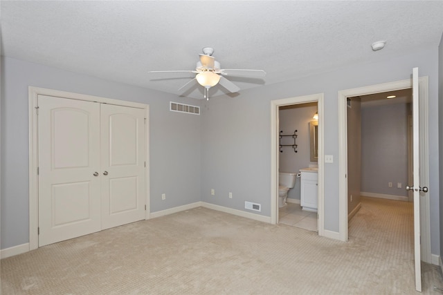 unfurnished bedroom with ensuite bathroom, light colored carpet, a textured ceiling, a closet, and ceiling fan