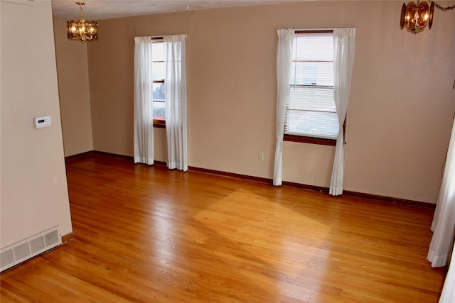 spare room with a wealth of natural light, visible vents, a notable chandelier, and light wood finished floors