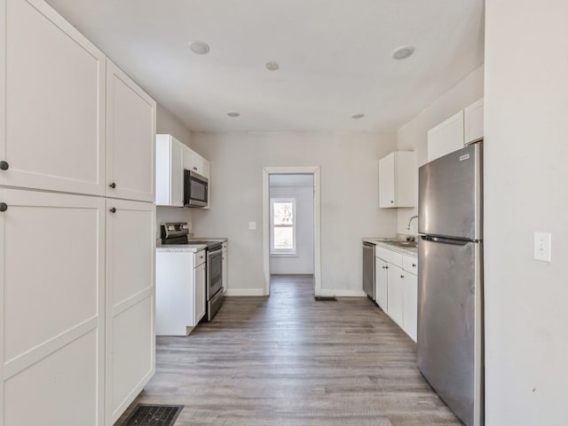 kitchen with sink, light hardwood / wood-style floors, white cabinets, and appliances with stainless steel finishes