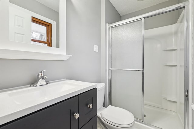 bathroom featuring toilet, vanity, a textured ceiling, and a shower with shower door