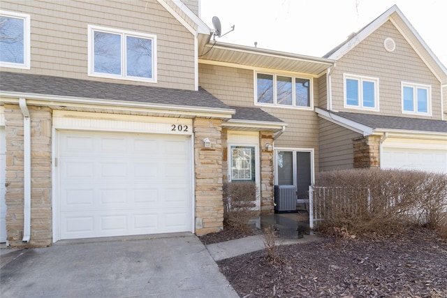 multi unit property with stone siding, central AC unit, roof with shingles, and an attached garage