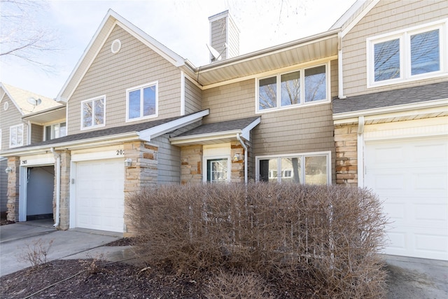 townhome / multi-family property with a garage, driveway, a shingled roof, stone siding, and a chimney