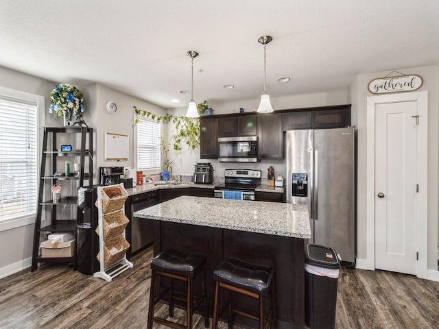 kitchen featuring a center island, appliances with stainless steel finishes, dark brown cabinets, and decorative light fixtures