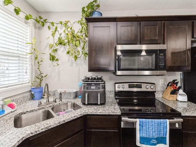 kitchen featuring sink, dark brown cabinets, stainless steel appliances, and light stone countertops