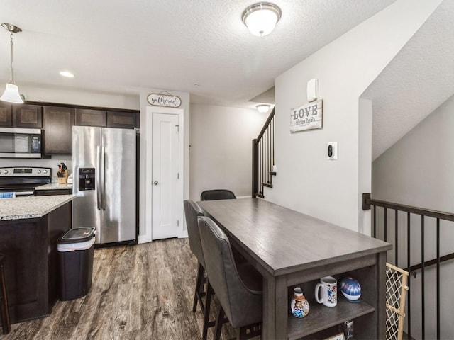 kitchen with dark brown cabinetry, light stone counters, decorative light fixtures, dark hardwood / wood-style floors, and stainless steel appliances