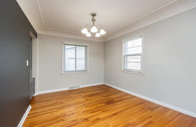 spare room with an inviting chandelier and light hardwood / wood-style floors