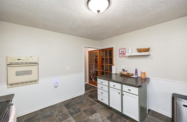 interior space featuring white cabinets, oven, and a textured ceiling