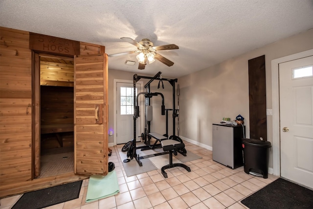 workout room featuring ceiling fan, light tile patterned floors, and a textured ceiling