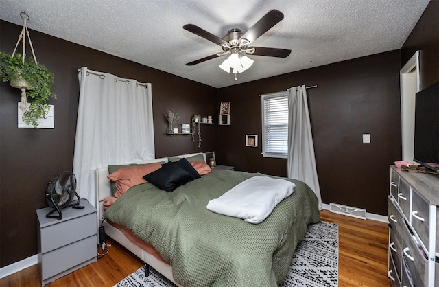 bedroom with ceiling fan, wood-type flooring, and a textured ceiling