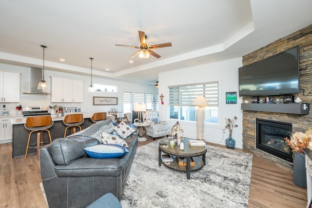 living room featuring ceiling fan, a fireplace, light wood-type flooring, and a tray ceiling