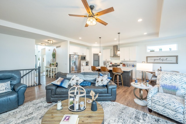 living room featuring a tray ceiling, ceiling fan, and light hardwood / wood-style flooring