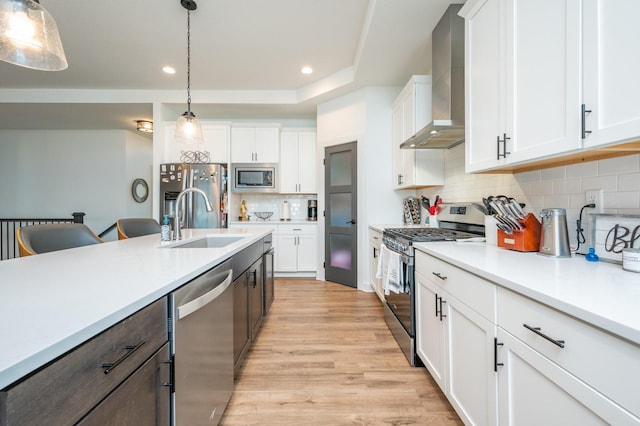 kitchen featuring appliances with stainless steel finishes, decorative light fixtures, white cabinetry, sink, and wall chimney range hood