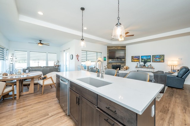 kitchen with sink, hanging light fixtures, a center island with sink, stainless steel dishwasher, and a raised ceiling