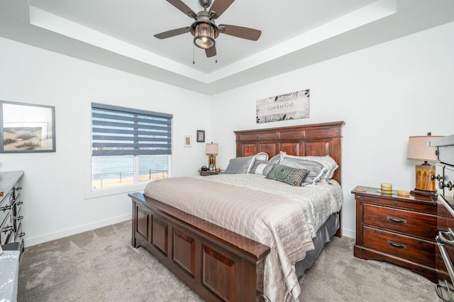 carpeted bedroom featuring a tray ceiling and ceiling fan