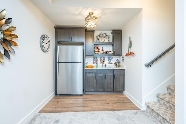 bar with stainless steel refrigerator, dark brown cabinetry, sink, and light wood-type flooring