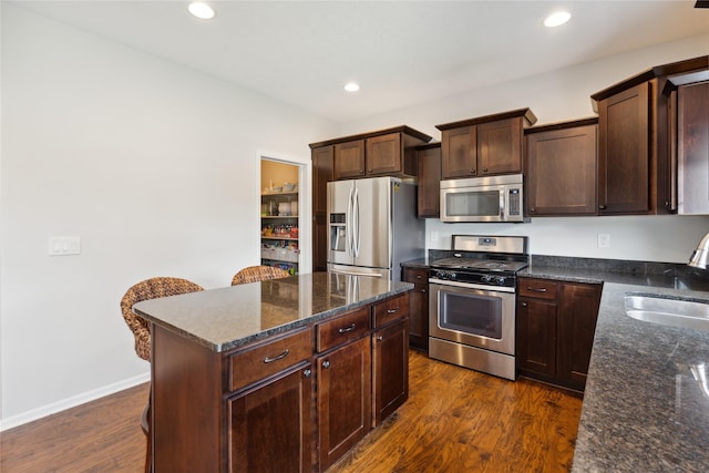 kitchen with dark wood-type flooring, sink, a center island, dark stone countertops, and appliances with stainless steel finishes