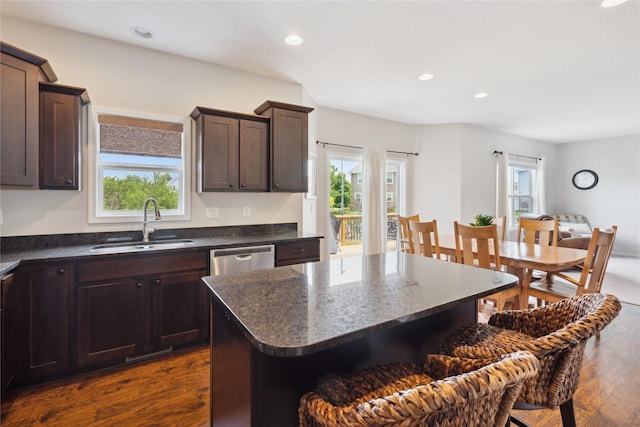 kitchen with dark wood-type flooring, sink, stainless steel dishwasher, a kitchen island, and dark stone counters