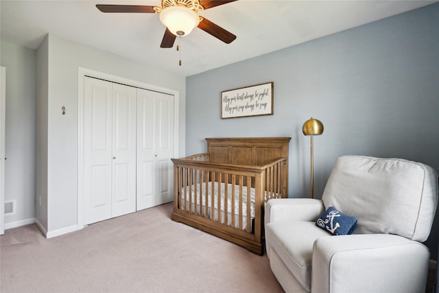 bedroom with ceiling fan, light carpet, a closet, and a crib