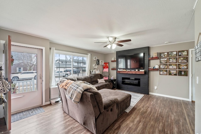 living room with ceiling fan, a textured ceiling, a fireplace, and light wood-type flooring