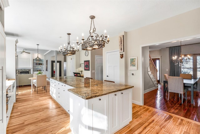 kitchen featuring pendant lighting, white cabinetry, dark stone countertops, a kitchen island, and light wood-type flooring