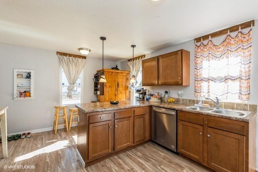 kitchen with sink, light wood-type flooring, stainless steel dishwasher, kitchen peninsula, and pendant lighting