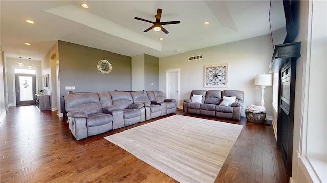 living room featuring dark hardwood / wood-style floors, ceiling fan, and a tray ceiling