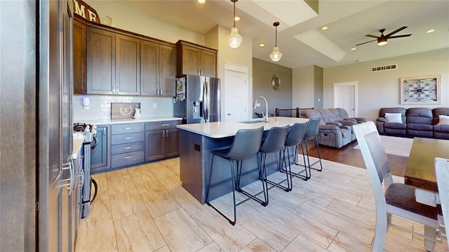 kitchen with pendant lighting, sink, stainless steel fridge, stainless steel refrigerator with ice dispenser, and an island with sink